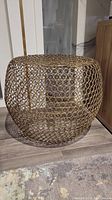 Front view of the gold metal wire ottoman showing full cylindrical lattice