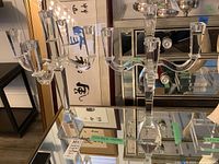 Photo showing two clear crystal candelabras on reflective glass surface, both with five arms for holding candles and faceted bases.