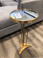 Front view of round mirrored top side table with gold-tone metal frame placed next to grey sofa