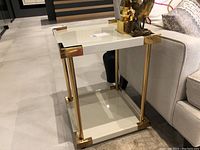 Front view of one side table beside sofa showing top and bottom shelves and gold frame