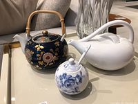Overview showing all three teapots: dark blue floral with bamboo handle, white modern curved teapot, and small blue floral teapot