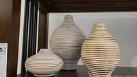Three ceramic vases with white and wood tone horizontal stripes arranged on a shelf.