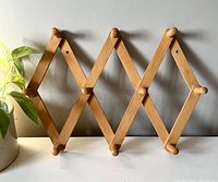 Front view of wooden accordion peg rack showing yellow-toned finish and 10 pegs in expanded position.