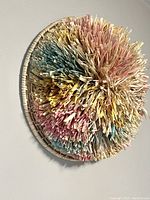 Front angled view showing textured colorful raffia in pastel pink, yellow, blue inside a round wicker frame.