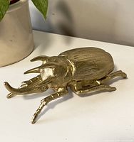 Front angled view of the gold beetle figurine showing the horns and leg details.