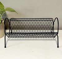 Front view of mid-century modern black metal book holder with diamond mesh and curved handles.
