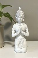 Front view of white Buddha statue, showing kneeling position, closed eyes, detailed clothing and accessories, matte finish.