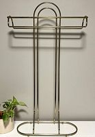 Full view of the vintage brass-toned towel rack standing upright against a white wall, showing the overall design and structure.