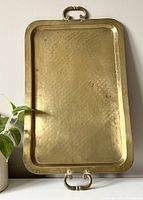 Full view of rectangular brass tray standing vertically showing stamped hammered surface and top and bottom handles.