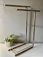 Vintage brass toned free standing towel rack shown from an angle, displaying four horizontal bars and wire rack base.