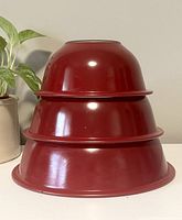 Stacked view of three vintage Pyrex mixing bowls showing their nesting design and red color.