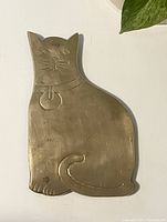 Front side of the cat-shaped brass trivet, showing engraved facial features and collar detail.