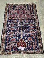 Top-down view of the entire hand knotted Blochi wool rug showing geometric and floral design on navy background.