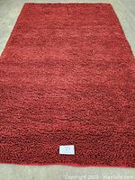 Full view of a deep red hand knotted hooked wool rug measuring 5x8 feet laid flat showing dense looped pile.