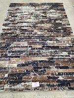 Full view of the large modern cowhide rug displaying a patchwork pattern with shades of brown, black, and cream on concrete background.