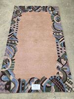 Full view of rectangular wool hand tufted rug with beige center and multicolor abstract geometric border.