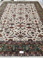 Full view of hand-knotted wool rug showing beige field with floral motifs and green border.