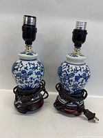 Front view of two vintage blue and white ceramic table lamps on dark wooden bases, with electrical sockets and cords coiled around the bases.