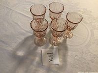 Photo showing a set of five pink sherry glasses with ribbed designs on the bowl, arranged with a lot number card.
