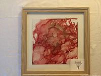 Framed abstract painting with red and pink fluid alcohol ink design, visible artist signature, displayed against neutral background.