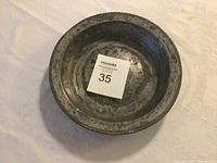 Top view of antique hammered metal plate with lot number card inside showing size and wear