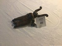 Brass boot jack captured from a side angle on a white fabric background with a lot card marked 46 beside it.