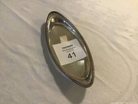 Silver oval-shaped serving tray with beaded rim on fabric background