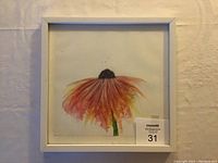 Framed alcohol ink artwork showing single flower in warm hues on white background with visible artist signature. Framed in simple white square frame, size approximately 12x12 inches.