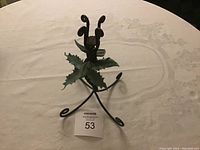Photo of the twisted metal candle holder showing three legs, curled upward ends and metal leaf decoration in center.