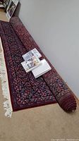 Rolled and partially unrolled hand knotted area rug on floor with fringe and packaging on top