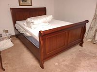 Front-left angle of mahogany-tone wooden sleigh bed with mattress, topper, cover, and duvet.