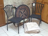 Two metal chairs, stacked cushions, round mosaic table top leaning, folded cover visible