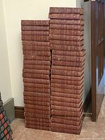 Photo showing two tall stacks of fifty hardcover books in brown covers, titles not visible.