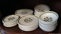Photo showing stacks of dinner plates, luncheon plates, dessert plates, and bowls with floral pattern and green rim.