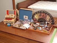 Overview of all lot items including jewellery box, assorted jewellery, fan, figurines, and vase on wooden surface