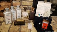 Photo of complete Lampe Berger box contents showing 2 lamps, 3 scent bottles, neutral fluid and wick box, placed on brick surface near firewood.