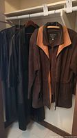 Three leather coats hanging on a closet rod showing full length styles and color variations.