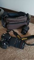 Overview showing brown camera bag, Nikon D3100 body with mounted Sigma lens and separate Nikkor 18-55mm lens