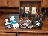 Wide view of the lot on wooden desk including calculator, cash box, pill cases, pens, and decorative items
