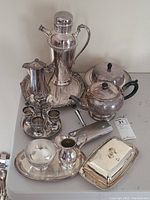 Photo showing the entire set arranged on a table, including coffee pot, teapot, hot water pitcher, tray, cream and sugar set, egg cup set, tablesweep, covered dish, and butter dish.
