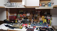 Wide view of the workspace with assorted hand tools on pegboard, jars of screws and nails, paint tray, brushes, and miscellaneous hardware items scattered on a surface.
