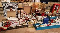 Wide shot showing multiple open boxes filled with various Christmas ornaments and decorations arranged on carpet in basement rec room in front of brick wall.