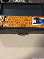 Open carrying case showing mah jongg tiles neatly arranged, with the National Mah Jongg League official rules card on top.