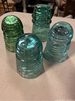 Set of four vintage glass insulators in various blue and green shades viewed from top-down angle