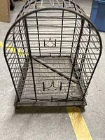 Front angle view showing the metal bars, wooden base, door hooks, and interior perch.