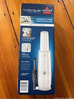 Front and side of the sealed box showing the Bissell Turboslim handheld vacuum with detailed features such as easy charging via USB cable, washable filter, and 2-in-1 crevice tool and dusting brush attachments.