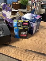 Overview of Eliminator fog machine box (damaged) and three new mini strobe light boxes on wooden table.