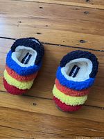 Pair of brightly colored toddler slippers with rainbow stripes from an overhead angle on a wooden surface.