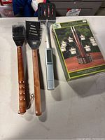 Full view of four items: two wooden-handled grilling tools (spatula, meat tenderizer), a digital thermometer, and boxed candle holder.
