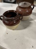 Photo of pair of ceramic bean pots, one with lid and one without, showing two-tone glaze and side handles.